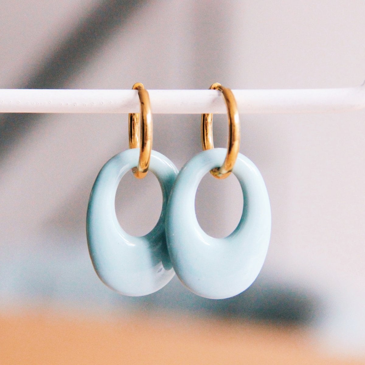 Bazou stainless steel earrings with blue resin teardrop, featuring gold accents, displayed on a white background.